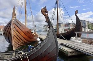 Prows of replica viking ships and medieval boats moored to the pier in the harbour of the small city of Tønsberg, Norway.